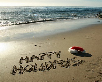 Happy Holidays written in sand with a Christmas hat beside, sea, from The Realty Medics