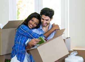 Young Couple - First Time Homeowners, black woman hugging his partner while the man is holding the box, a lot of boxes around them