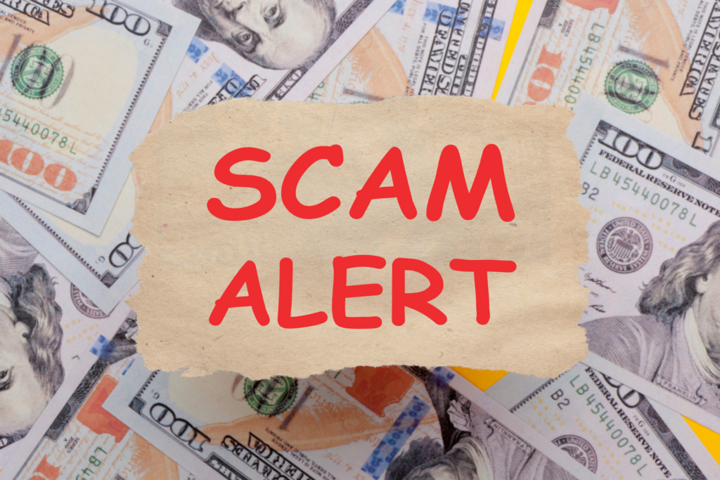 A pile of 100 hundred dollar bills with a digital torn piece of paper with the words “scam alert” hovering over the bills.