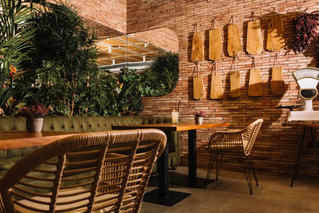 A rustic restaurant with a brick wall, mirror, wooden tables and chairs, olive couch, and lush plants, showcasing the best bars and restaurants in Orlando.