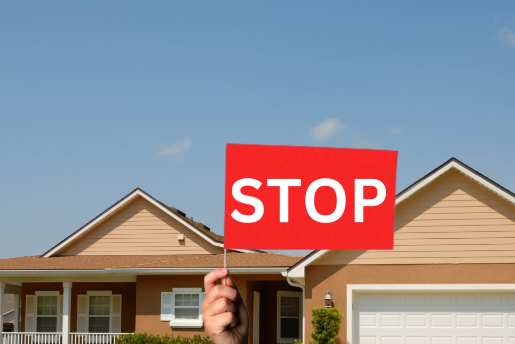 Hand holding a red flag with the word 'Stop' in the foreground, representing tenant screening red flags, with the top of a yellow house in the background.