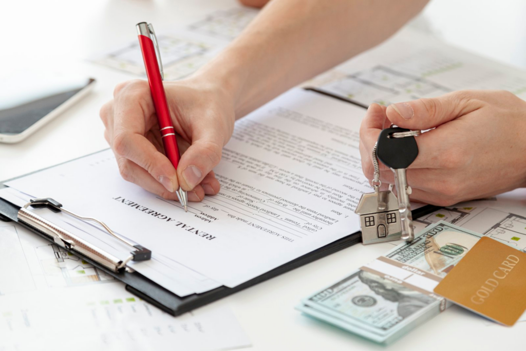 Hands signing an Orlando lease renewal with a red pen on the right, while holding a key with a house keychain on the left. Under the left hand are a few dollars and a gold credit card.